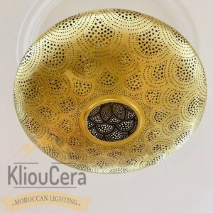 May include: A gold-coloured, round, metal ceiling light fixture with a decorative, intricate, cut-out pattern. The light fixture is hanging from a white ceiling.
