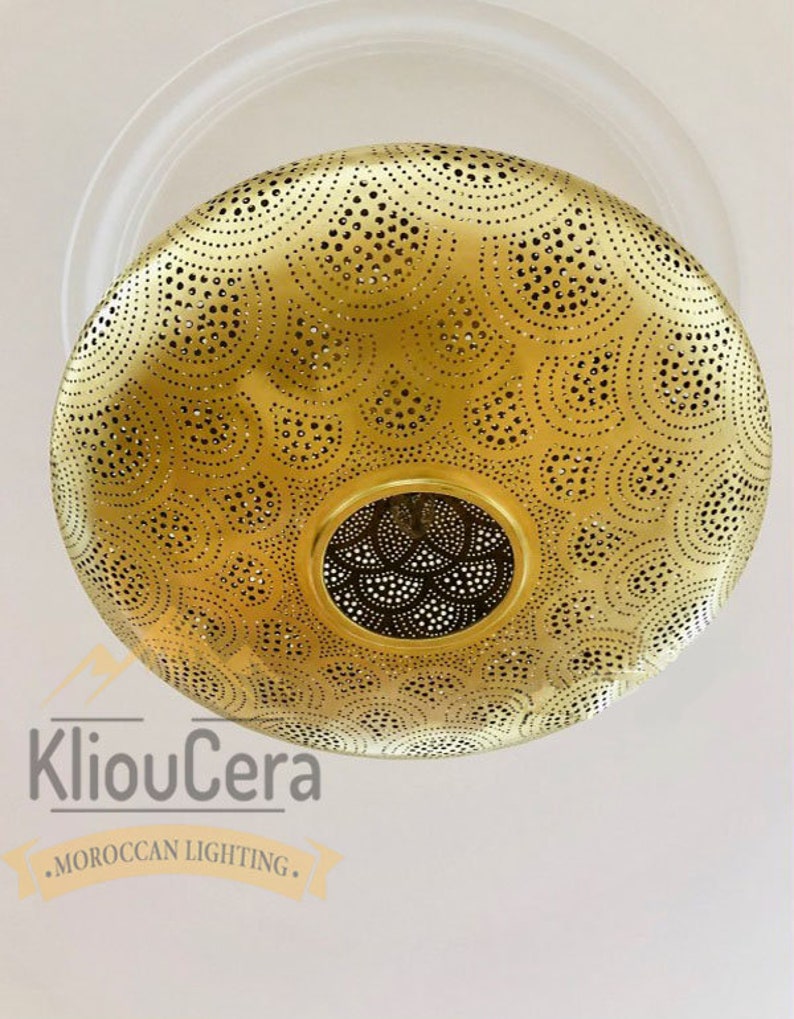 May include: A gold-coloured, round, metal ceiling light fixture with a decorative, intricate, cut-out pattern. The light fixture is hanging from a white ceiling.