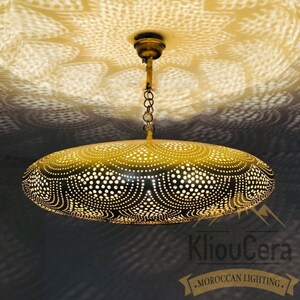 May include: A gold-coloured, oval-shaped pendant light fixture with a decorative, intricate pattern of small holes. The light fixture is hanging from a chain and is casting a patterned shadow on the ceiling.