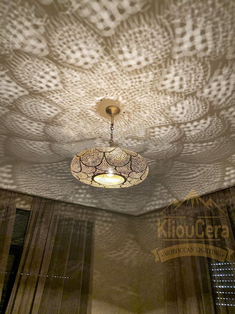 May include: A round, brass Moroccan pendant light fixture with intricate cut-out designs. The light casts a patterned shadow on the ceiling. The fixture is hanging from a chain and has a decorative ceiling mount.