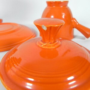 May include: Orange ceramic lid with a knob on top. The lid has a glossy finish and is slightly domed.