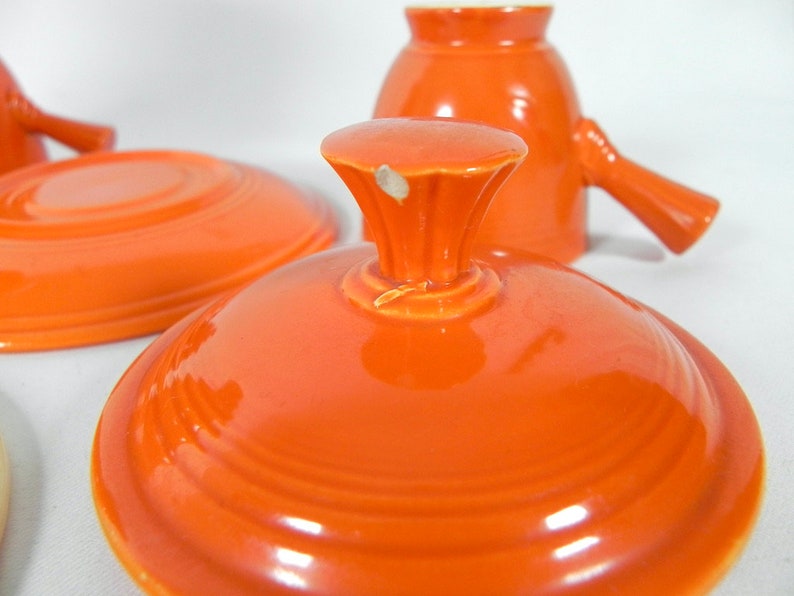 May include: Orange ceramic lid with a knob on top. The lid has a glossy finish and is slightly domed.