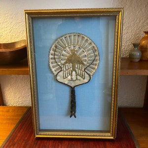 May include: A framed peacock fan with gold and blue accents, displayed on a blue background.