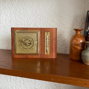 May include: A wooden barometer and thermometer in a gold frame. The barometer has a dial with the words "FRANKE & LUST" and "SCHUTT" printed on it. The thermometer is in Celsius and reads from 0 to 4 degrees.