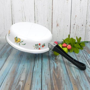 May include: White enamel oval-shaped frying pan with a black handle. The pan features a floral design with lemons, strawberries, and leaves.