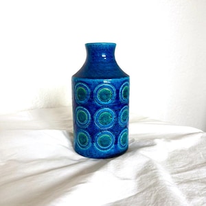 Peut inclure: Un vase en céramique bleu avec un corps cylindrique et un col étroit. Le vase est décoré d'un motif de cercles bleu et turquoise. Le vase mesure environ 20 cm de haut.