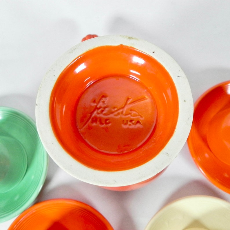 May include: A set of four Fiestaware dinner plates in various colors, including orange, green, and cream. The bottom of the orange plate shows the Fiestaware logo with "Made in USA" printed on it.