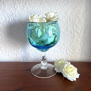 May include: A blue glass vase with a twisted stem, filled with white silk roses.