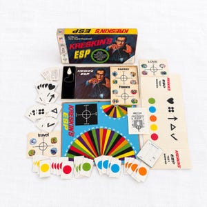 Könnte beinhalten: Kreskin's ESP Brettspiel-Set mit gelbem Karton, einem Spielbrett mit farbigem Radialdesign und Alphabet, einem Pendel, verschiedenen Spielkarten mit Symbolen und Farben, Anleitungsheften sowie Testbildschirmen mit aufgedrucktem Text.