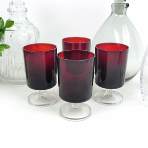 Può includere: Set di quattro bicchieri da vino rosso con steli e basi trasparenti. I bicchieri hanno un gradiente dal rosso scuro al rosso chiaro.