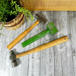 Può includere: Tre martelli con manici in legno. Un martello ha una testa verde, uno ha una testa nera e uno ha una testa argentata.