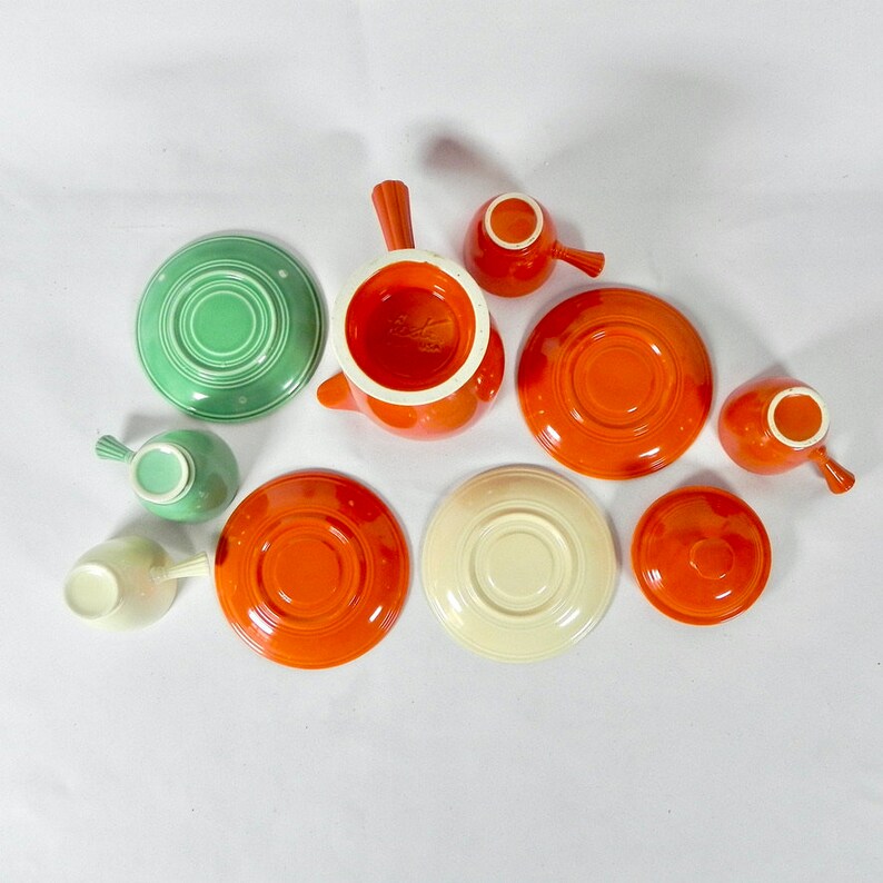 May include: A set of vintage orange and green ceramic teacups and saucers. The set includes a teapot, a creamer, and six cups and saucers.