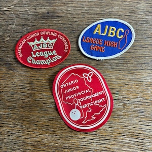 May include: Three vintage bowling patches. One red patch reads "American Junior Bowling Congress League Champion". A blue patch says "AJBC League High Game". A red patch reads "Ontario Junior Provincial Tournament Participant".