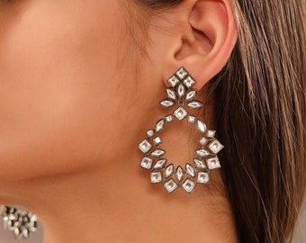 May include: A pair of silver dangle earrings with a circular design. The earrings are adorned with clear, faceted stones.