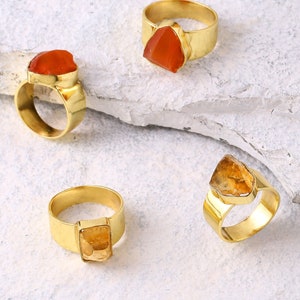 May include: Four gold rings with different colored gemstones. The rings are on a white background.