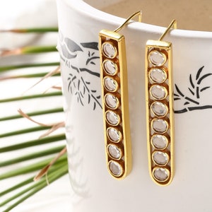 May include: Gold dangle earrings with clear round stones set in a rectangular frame.