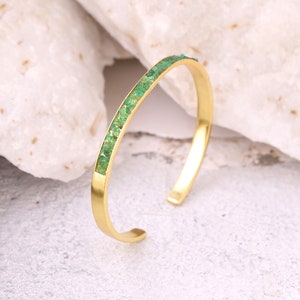 May include: A gold bangle bracelet with a band of green emerald gemstones.