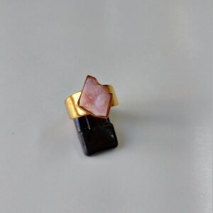 May include: A gold ring with a pink, irregular shaped stone set in the center.