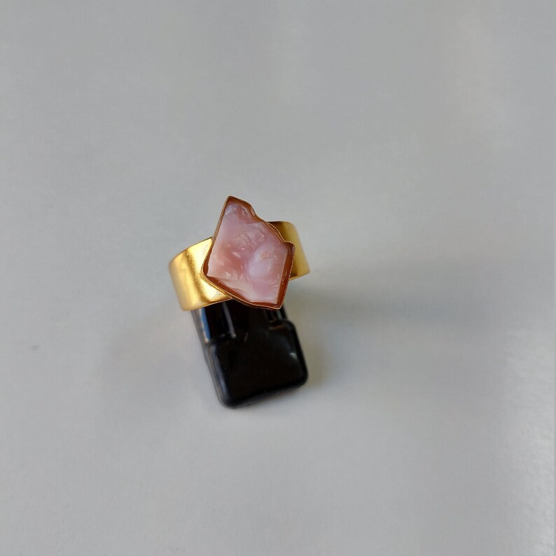 May include: A gold ring with a pink, irregular shaped stone set in the center.