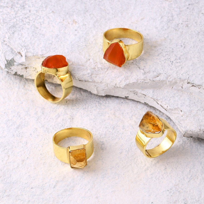 May include: Four gold rings with different colored gemstones. The rings are on a white background.