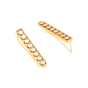 May include: A pair of gold earrings with a row of clear round stones. The earrings are long and thin, and the stones are set in a gold frame.