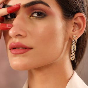 May include: Gold earrings with a vertical design featuring clear round stones. The earrings are a simple and elegant design.