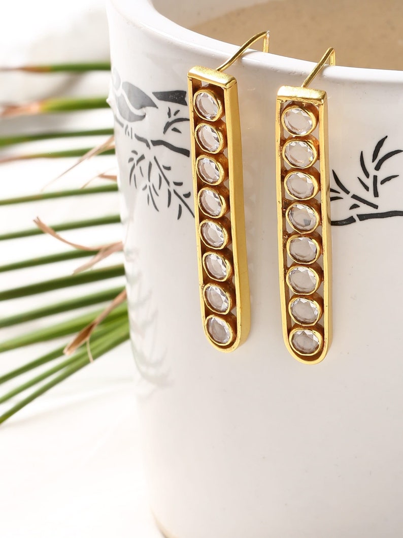 May include: Gold dangle earrings with clear round stones set in a rectangular frame.