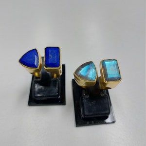 Pu&ograve; includere: Due paia di anelli d'oro con pietre preziose blu e verdi. Gli anelli sono esposti su supporti neri.