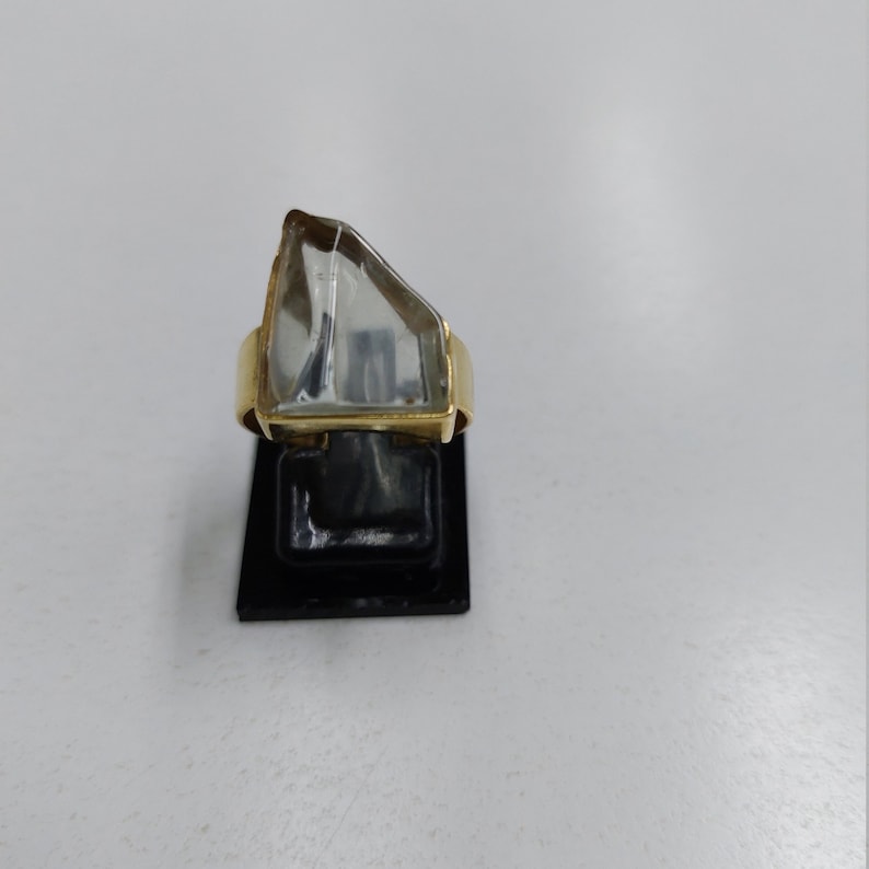 May include: A gold ring with a clear, faceted gemstone. The gemstone is set in a gold bezel and the ring band is plain.