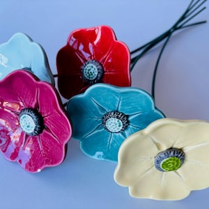 Puede incluir: Cinco flores de cerámica en tonos de azul, rojo, rosa y amarillo. Las flores están dispuestas en un ramo y tienen un aspecto realista.