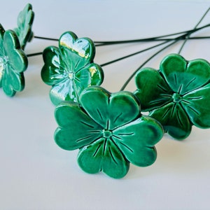 Puede incluir: Cinco flores de cerámica verde con tallos de alambre. Las flores tienen cinco pétalos cada una y un centro elevado.