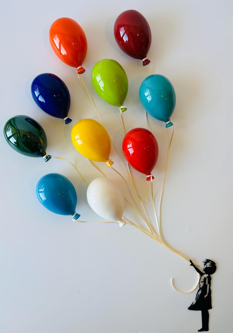 May include: A collection of eleven glossy, colorful balloons in shades of orange, red, green, blue, yellow, and white. The balloons are held by a silhouette of a child, creating a whimsical and artistic display.