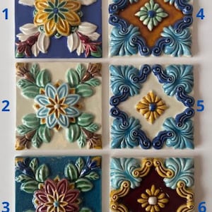 May include: Six square ceramic tiles with floral designs. Each tile features a raised, colorful pattern of flowers and leaves in shades of blue, yellow, green, white, and burgundy. The tiles are arranged in a grid.