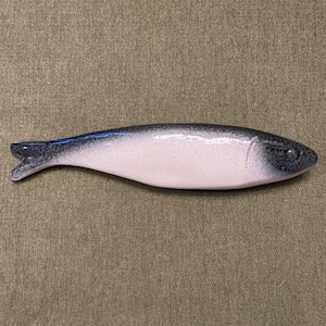 May include: A ceramic fish shaped dish with a white glaze and black detailing. The dish is a light pink colour and has a slightly curved shape.