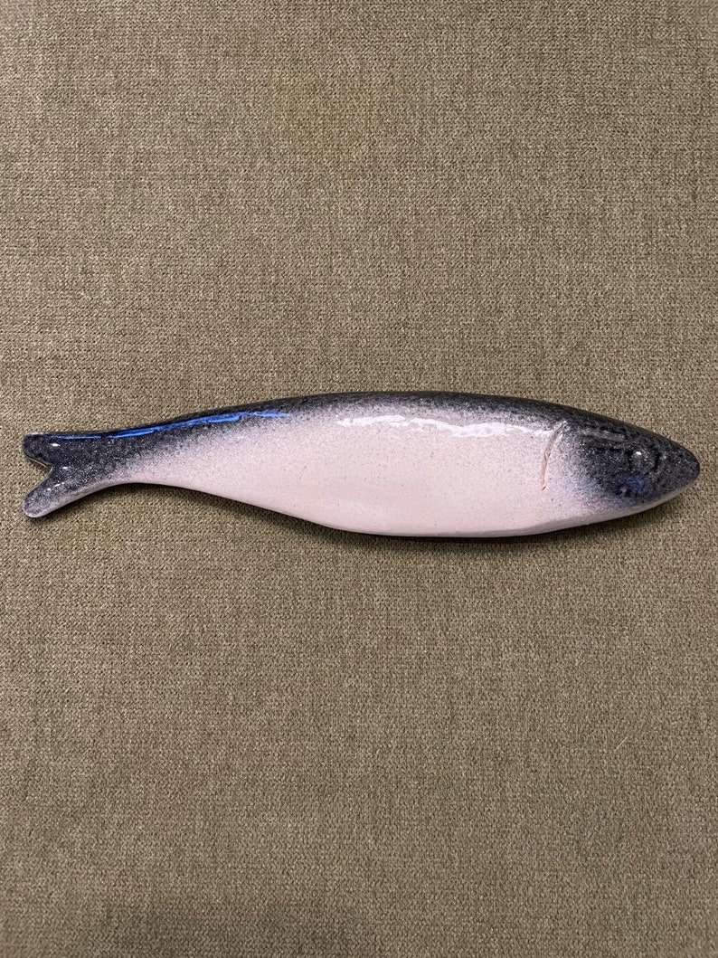 May include: A ceramic fish shaped dish with a white glaze and black detailing. The dish is a light pink colour and has a slightly curved shape.