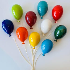 May include: A cluster of ten glossy, colorful balloon-shaped ornaments. The balloons are in various shades, including blue, green, red, orange, yellow, and white. Each balloon has a string attached, creating a festive and decorative arrangement.
