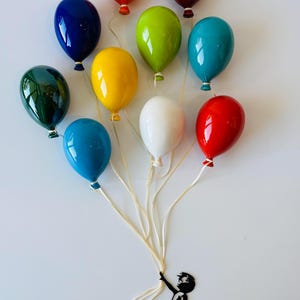 May include: A colorful wall art piece featuring a cluster of glossy, balloon-shaped sculptures in various colors, including red, blue, and green. A silhouette of a child holding the balloon strings is attached to the wall.
