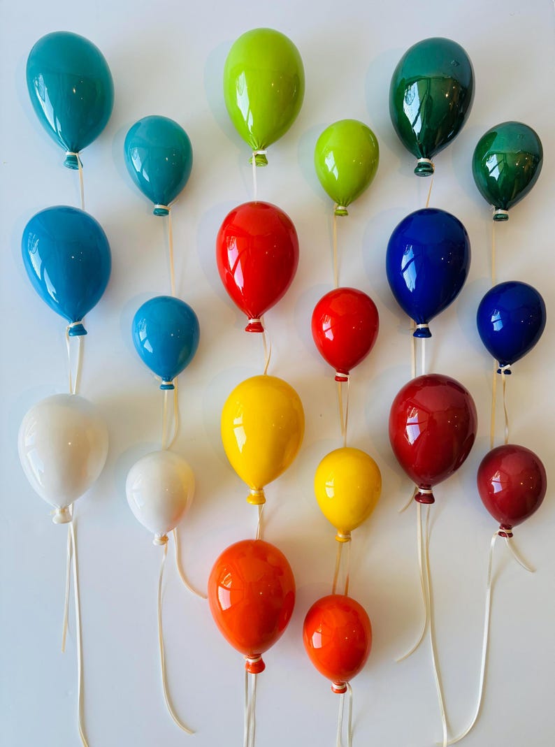 May include: A collection of glossy, colorful balloon-shaped decorations in various sizes. The balloons are in shades of teal, green, red, blue, white, yellow, and orange, each with a white string. They are arranged against a white background.