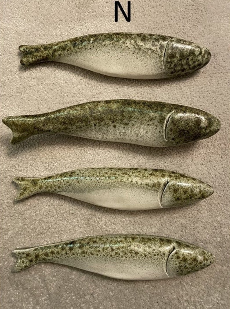 May include: Four ceramic fish figurines in a green and white speckled glaze. The fish are arranged in a row, with their tails pointing to the right. The fish are all the same size and shape, and they have a slightly curved body. The fish are a decorative item for a home or office.