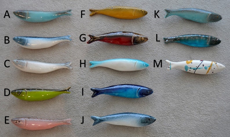 May include: Twelve ceramic fish figurines in various colours and patterns, including blue, green, red, yellow, and white. The fish are arranged in four rows of three, with letters A through M labelling each fish.