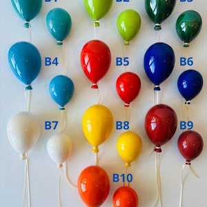 May include: A collection of colorful, glossy balloon ornaments in various sizes and shades, including teal, green, red, blue, yellow, and white. Each balloon is suspended by a thin, white string, creating a festive and decorative display.