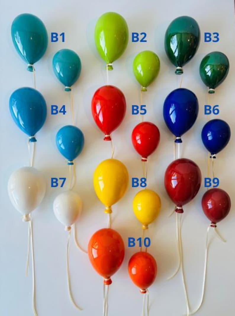 May include: A collection of colorful, glossy balloon ornaments in various sizes and shades, including teal, green, red, blue, yellow, and white. Each balloon is suspended by a thin, white string, creating a festive and decorative display.