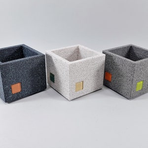 May include: Three square-shaped planters made of a textured gray material. The planters have a small square of color on each side: blue, green, and yellow.