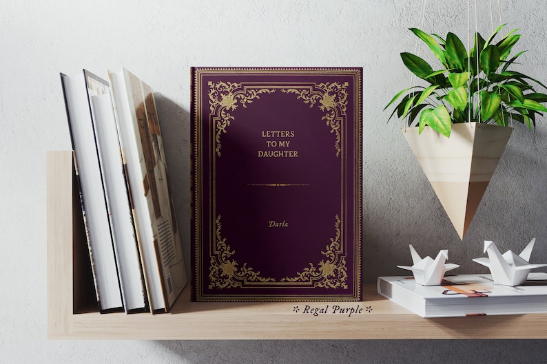 May include: A purple book with gold lettering and a decorative gold frame on the cover. The title of the book is "Letters to My Daughter" and the author is "Darla". The book is on a wooden shelf with other books and decorative items.