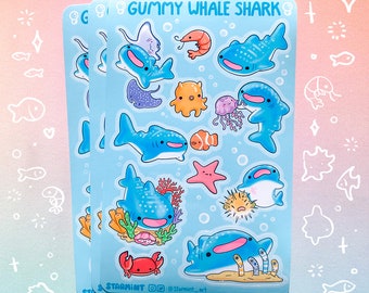 May include: A set of three sticker sheets featuring a variety of cute, cartoon-style whale sharks, sea creatures, and coral reefs. The sticker sheets are blue with white outlines and the text "GUMMY WHALE SHARK" at the top. The sticker sheets are designed by "STARMINT" and include the social media handle "@starmint_art".