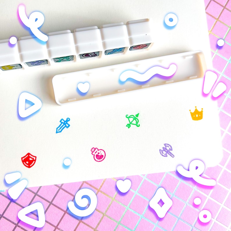 May include: A white organizer with a row of small, colorful, illustrated icons. The icons include a sword, bow and arrow, shield, potion, and axe. The background is a white surface with a pink and iridescent grid pattern.