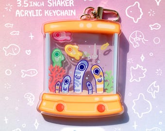 May include: A 3.5-inch acrylic shaker keychain featuring a whimsical aquarium design. The keychain has an orange frame and contains colorful fish, coral, and other aquatic elements. The word "FRONT" is printed at the bottom.
