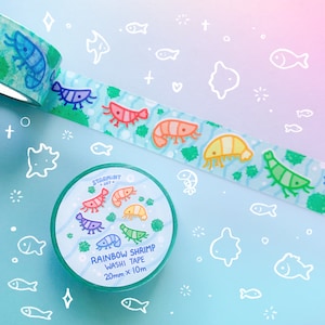 Puede incluir: Un rollo de cinta washi con un dise&ntilde;o de camarones arco&iacute;ris. La cinta tiene 20 mm de ancho y 10 m de largo. La cinta est&aacute; sobre un fondo blanco con un degradado azul y rosa.