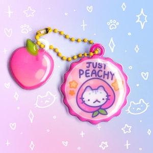 May include: A pink keychain with a peach charm and a circular charm with a cat inside a peach, the text "JUST PEACHY", and star graphics. The charms are connected by a yellow beaded chain.