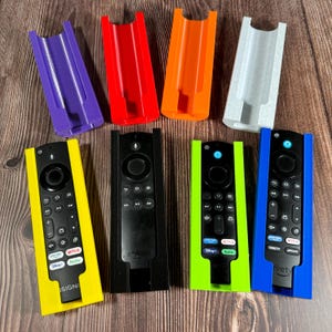 May include: Six different colored 3D printed wall mounts for remote controls. The mounts are designed to hold a variety of remote controls, including those for Amazon Fire TV and Roku. The mounts are shown with different colored remote controls.